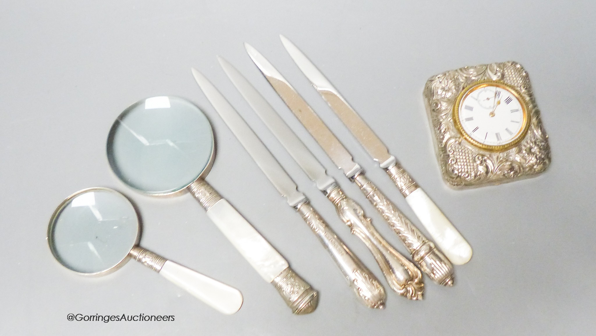 A group of mixed silver to include a travelling timepiece, mother of pearl handled knives, an eyepiece, etc.